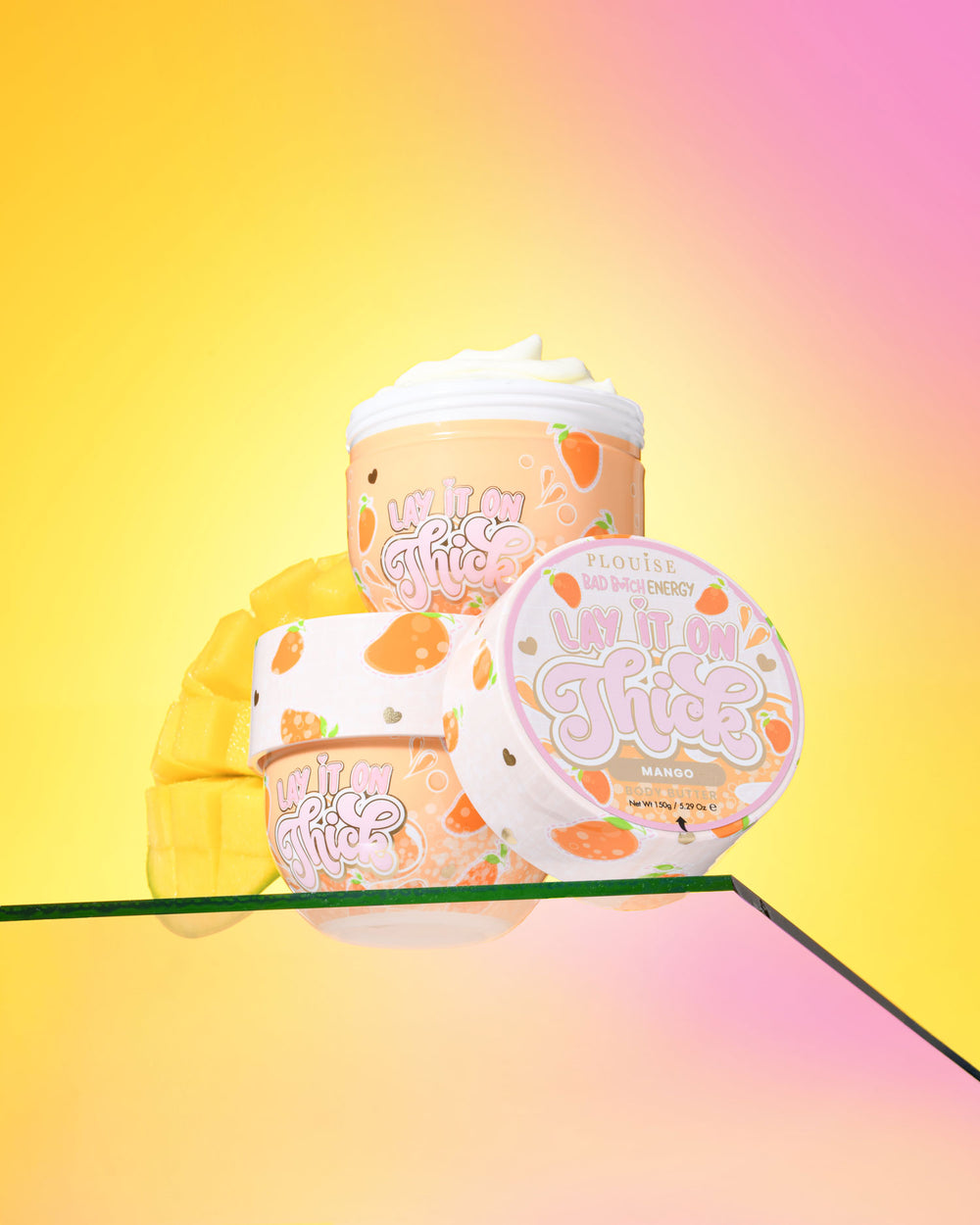 Three containers of P. Louise 'Lift It On Thick' mango body butter on a gradient yellow and pink background