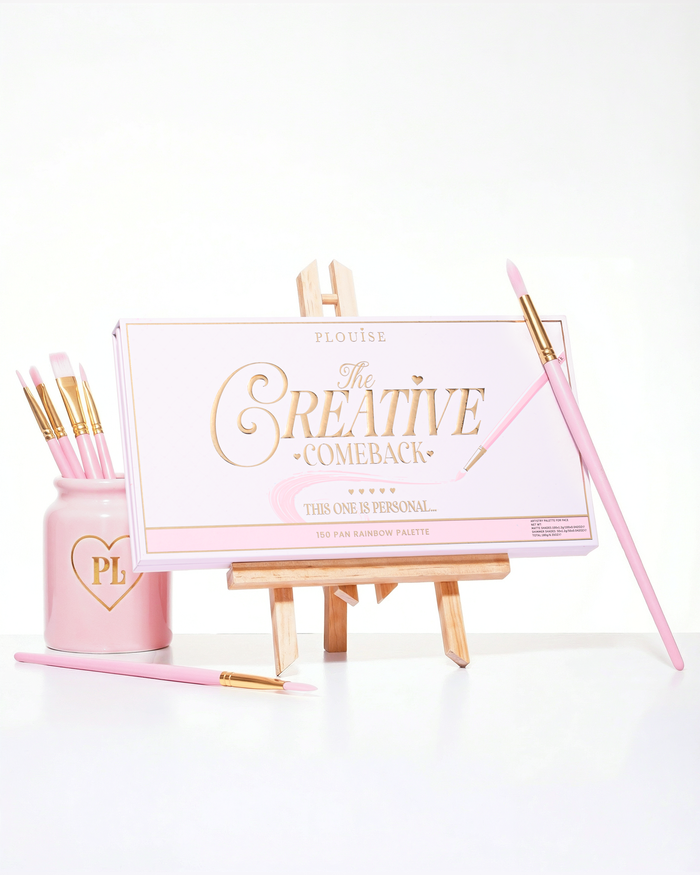 封闭式粉色 P.Louise Creative Comeback XXXL 彩虹眼影盘放置在艺术画架上，四周环绕着化妆刷