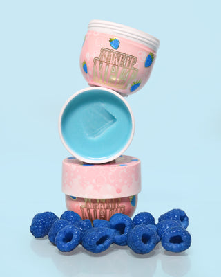 3 tubs of P. Louise Make It Melt Makeup Removing Cleansing Balm in blue raspberry on top of each other with the middle one open showing blue cream surrounded by blue raspberries on a blue background