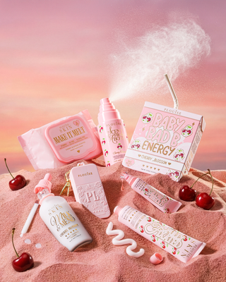 Collection of pink and white cherry blossom skincare products with cherry elements on a pink background on top of sand