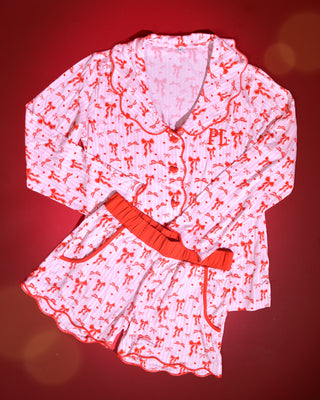 Image of pink and white striped christmas adults pyjamas with red bow designs on a red background